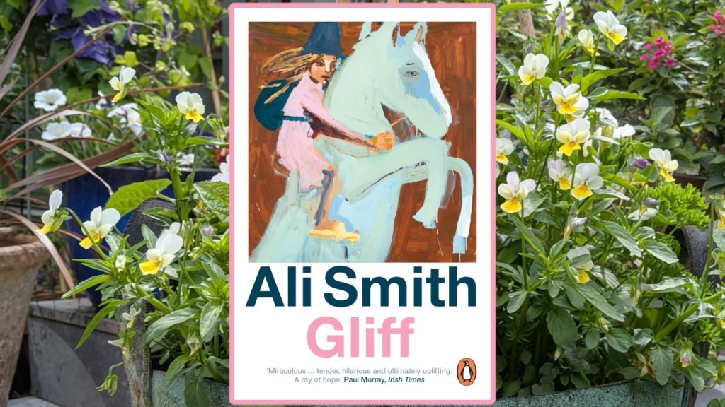 Gliff by Ali Smith cover over a pot filled with soft white viola